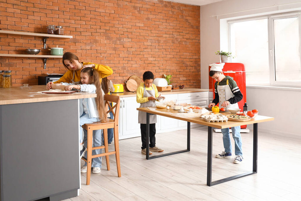 Female chef with group of little children preparing pizza during cooking class in kitchen - Fotografie, Obrázek