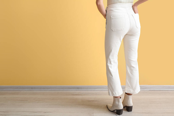 Mujer joven en jeans blancos cerca de la pared amarilla, vista trasera - Foto, imagen