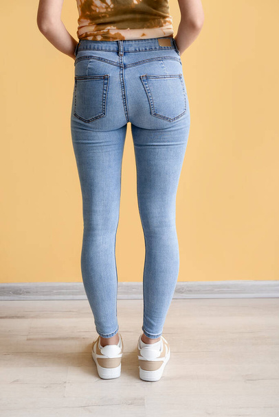 Young woman in stylish jeans near yellow wall, back view - Foto, Imagem
