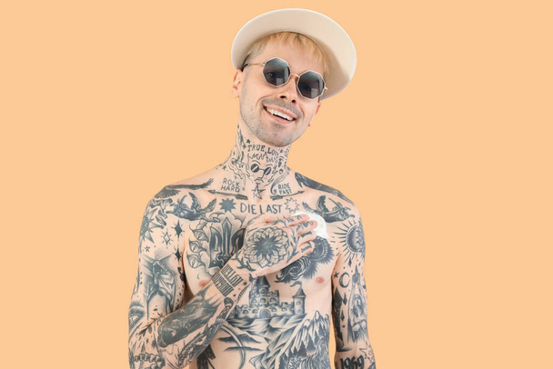 Татуированный мужчина наносит крем от загара на бежевый фон - Фото, изображение