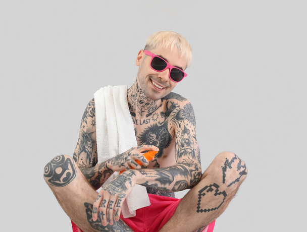 Tattooed man applying sunscreen cream on light background - Photo, Image