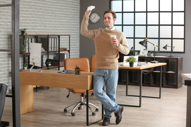 Mladý muž s papírem letadlo a šálek kávy v kanceláři - Fotografie, Obrázek