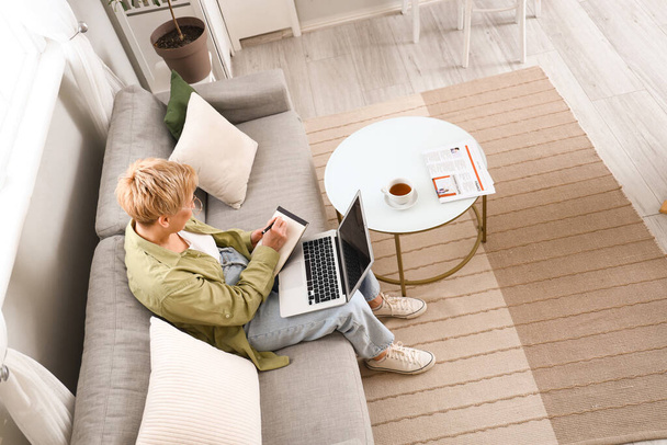 Programmatrice matura che lavora con laptop e notebook sul divano di casa - Foto, immagini
