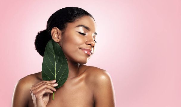 Happy woman, leaf and natural beauty in studio, pink background and mockup for aesthetic cosmetics. Face, african model and skincare from plants, green leaves and sustainability of vegan dermatology. - Photo, Image