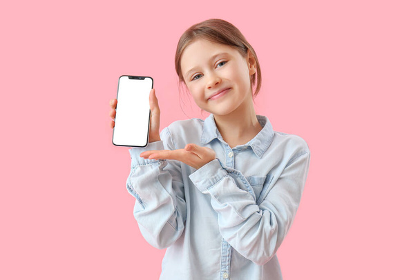 Маленькая девочка с мобильным телефоном на розовом фоне - Фото, изображение