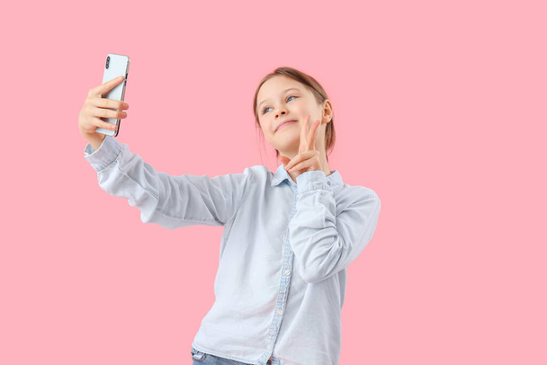 Маленькая девочка с мобильным телефоном видео чата на розовом фоне - Фото, изображение