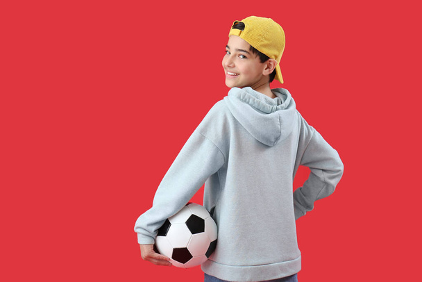 赤い背景にサッカーボールを持つ小さな男の子 - 写真・画像