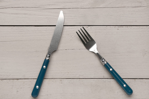 Stainless steel fork and knife with blue handles on grey wooden background - Foto, Imagem