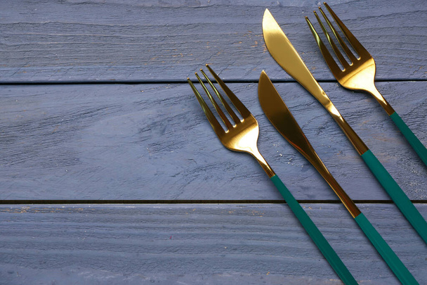 Zlaté vidlice a nože s barevnými rukojetěmi na modrém dřevěném pozadí - Fotografie, Obrázek