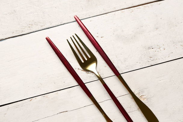 Złoty widelec i noże z czerwonymi rączkami na białym drewnianym tle - Zdjęcie, obraz