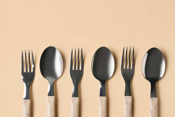 Stainless steel forks and spoons with plastic handles on beige background - Фото, зображення
