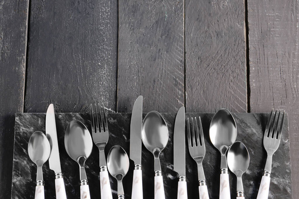 Board with stainless steel cutlery on black wooden background - Fotoğraf, Görsel