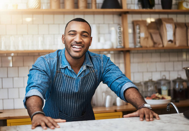 Koffieshop, barista en gelukkig portret van de zwarte man in restaurant voor service, werken en welkom in cafe. Kleine ondernemer, bistro startup en mannelijke ondernemer glimlach door teller klaar om te dienen. - Foto, afbeelding
