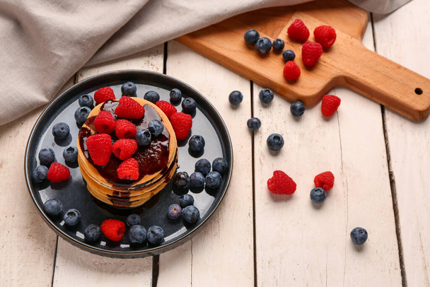 Teller mit süßen Pfannkuchen und Beeren auf hellem Holzhintergrund - Foto, Bild