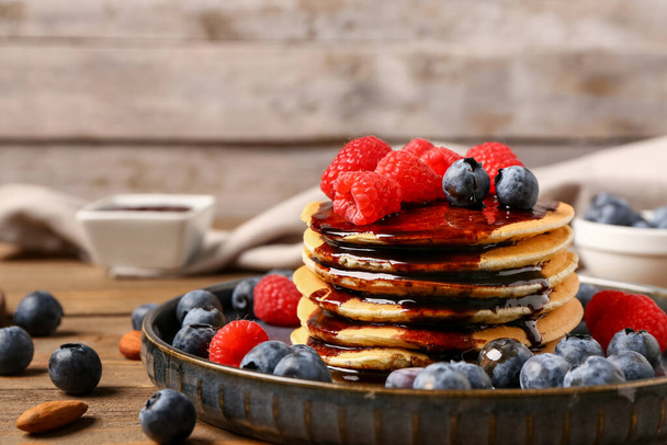 Plate with sweet pancakes, nuts and berries on wooden table, closeup - Valokuva, kuva