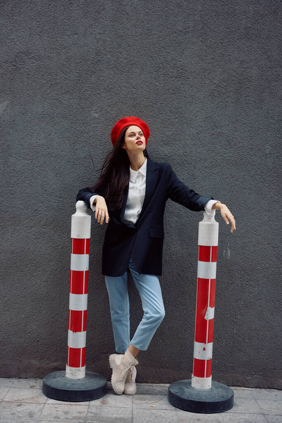 Módní žena stojící na ulici před městem a silnicí pracuje turista ve stylovém oblečení s červenými rty a červeným baretem, cestování, filmová barva, retro vintage styl. Kvalitní fotografie - Fotografie, Obrázek