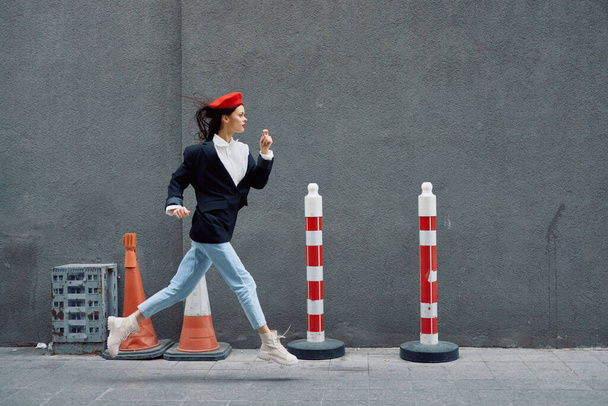Mujer de moda corriendo por la calle frente al turista de la ciudad en ropa elegante con labios rojos y boina roja, viajes, color cinematográfico, estilo vintage retro, tarde al trabajo. Foto de alta calidad - Foto, Imagen