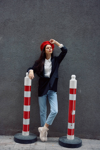 Módní žena stojící na ulici před městem a silnicí pracuje turista ve stylovém oblečení s červenými rty a červeným baretem, cestování, filmová barva, retro vintage styl. Kvalitní fotografie - Fotografie, Obrázek