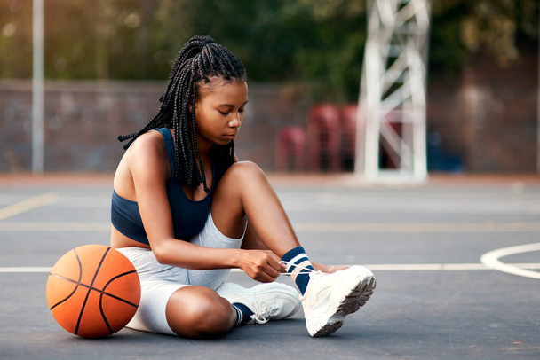 Kaksoissolmioni on aina turvallinen. viehättävä nuori urheilija istuu kentällä ja sitoo kengännauhansa ennen koripalloa - Valokuva, kuva
