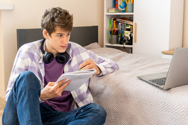 Jeune adolescent concentré avec ordinateur portable sur le canapé à la maison. Le garçon fait ses devoirs avec un ordinateur. Distance, éducation en ligne pour les enfants - Photo, image