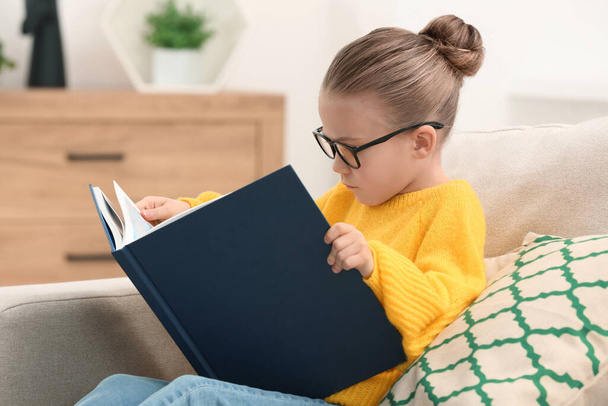 Cute little girl in glasses reading book indoors - Foto, Imagem