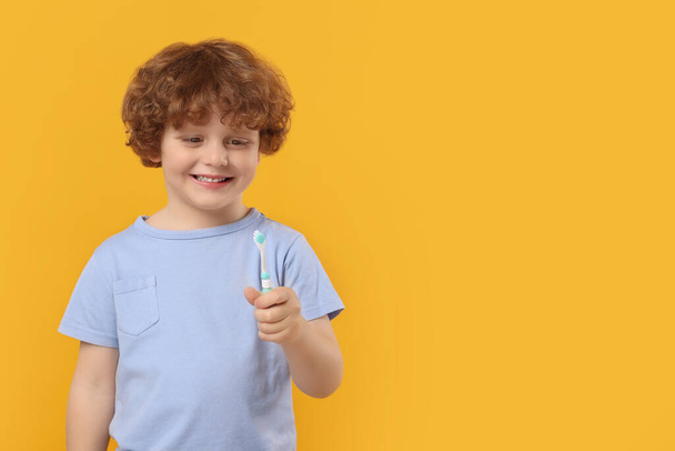 Cute little boy holding plastic toothbrush on yellow background, space for text - Fotoğraf, Görsel