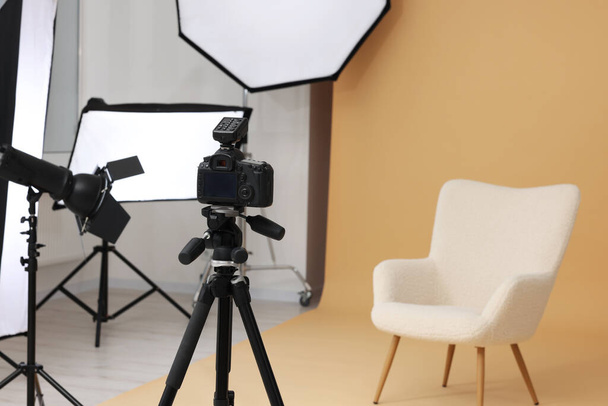Camera on tripod, armchair and professional lighting equipment in modern photo studio, space for text - Φωτογραφία, εικόνα