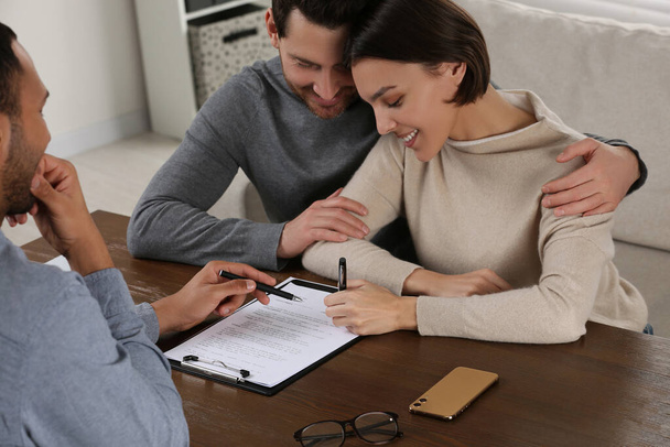 Professional notary helping couple with paperwork at wooden table - Photo, Image