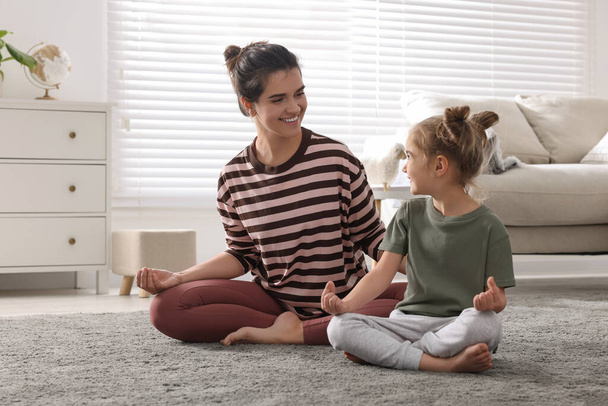 Young mother and her daughter meditating together at home - Foto, afbeelding