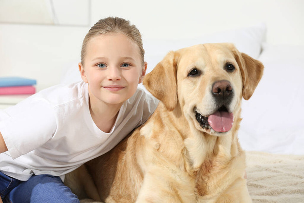 Cute child with her Labrador Retriever on bed at home. Adorable pet - Fotografie, Obrázek