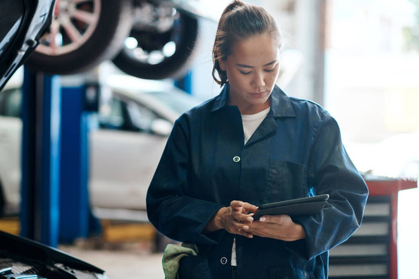 Lassen Sie sich von uns ein detailliertes Angebot zu Ihrem Fahrzeug zusenden. eine Mechanikerin hält ein digitales Tablet in der Hand, während sie in einer Autowerkstatt arbeitet - Foto, Bild