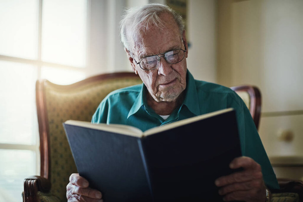 Beurteilen Sie ein Buch nie nach seinem Einband. ein älterer Mann liest ein Buch, während er sich zu Hause entspannt - Foto, Bild