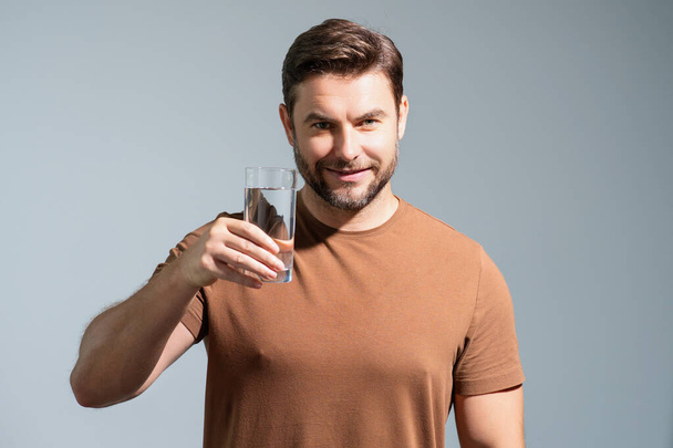 Man drinking fresh water. Male model holds glass of clear water. Healthy lifestyle, health care. Mineral water refreshment, daily dose of clean aqua, dehydration. Portrait of man drinking water - Zdjęcie, obraz