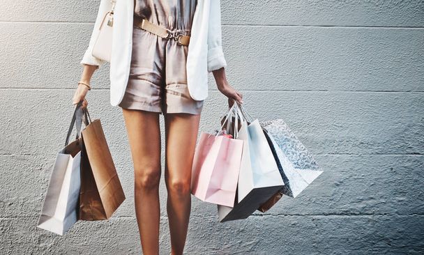 Shopping bag, legs and woman isolated by a wall background for retail, fashion and sale, deal or promotion. Rich, wealth and discount of person or clothes customer with gift bags outdoor or in city. - Fotoğraf, Görsel