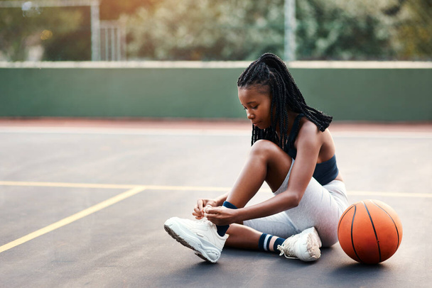 Bağcıklarımın sıkıca bağlı olduğundan emin oluyorum. Basketbol oynamadan önce sahada oturan ve ayakkabı bağcıklarını bağlayan çekici bir genç bayan. - Fotoğraf, Görsel