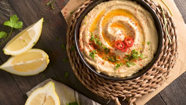 Delicious hummus in ceramic bowl. Colorful snack composition on a black wooden background. - Fotoğraf, Görsel