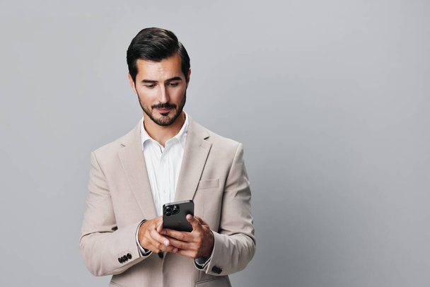 счастливый человек киберпространство бизнес-бежевый интернет уверенный предприниматель портрет сотовый корпоративный звонок изолированный костюм улыбка смартфон парень держать серый телефон - Фото, изображение