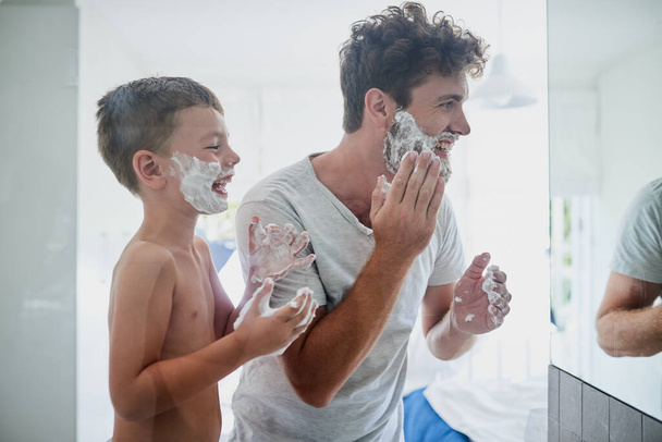 Kid, father and learning to shave, laughing and bonding together in bathroom. Funny, dad and teaching child with shaving cream on face beard, playing or cleaning, hygiene or enjoying hair removal - Fotografie, Obrázek