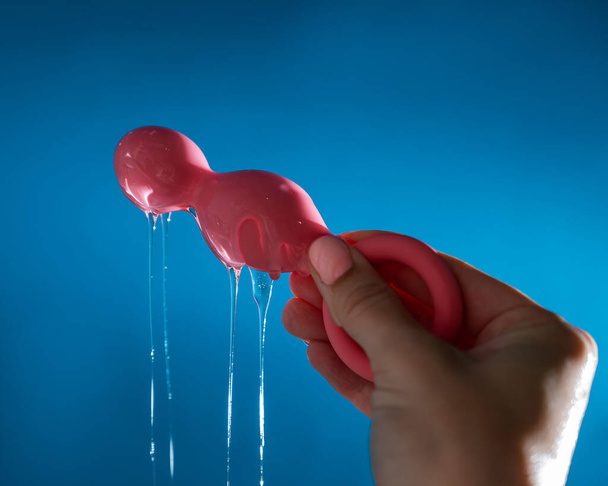 Mujer vertiendo lubricante sobre cuentas anales de color rosa sobre fondo azul - Foto, Imagen