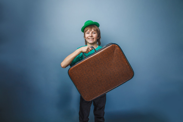Europese uitziende jongen van tien jaar met een koffer in een hoed op een - Foto, afbeelding