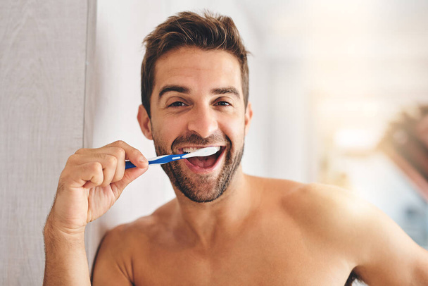 Aliento fresco para un día fresco. Retrato recortado de un joven guapo cepillándose los dientes en su baño en casa - Foto, imagen