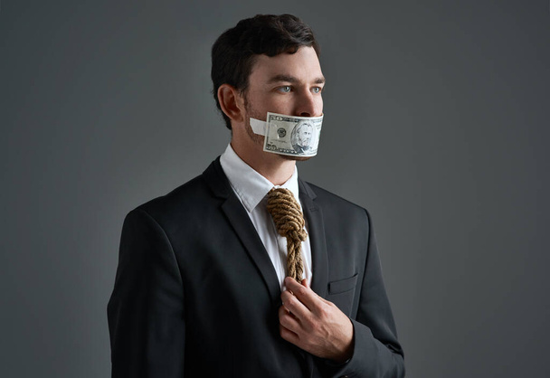 Де мораль на бізнес-ринку. Студійний знімок бізнесмена з мотузкою на шиї і грошима, заклеєними йому в рот на сірому фоні
 - Фото, зображення