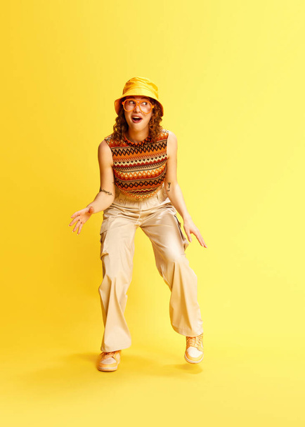 Retrato completo de jovem alegre em roupa elegante posando contra o fundo do estúdio amarelo. Humor positivo. Conceito de emoções engraçadas meme, cultura da juventude, moda, estilo de vida - Foto, Imagem