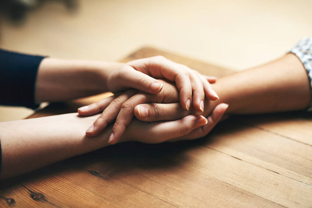 Holding hands, cancer and support of friends, care and empathy together on table in home mockup. Kindness, love and women hold hand for hope, trust or prayer, comfort or compassion, help or unity - Foto, Bild
