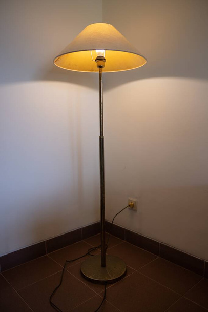 Interior con lámpara de pie y bombilla de resplandor en la oscuridad por la noche, una lámpara en la esquina contra una pared de lámpara de pie. Foto de alta calidad - Foto, Imagen