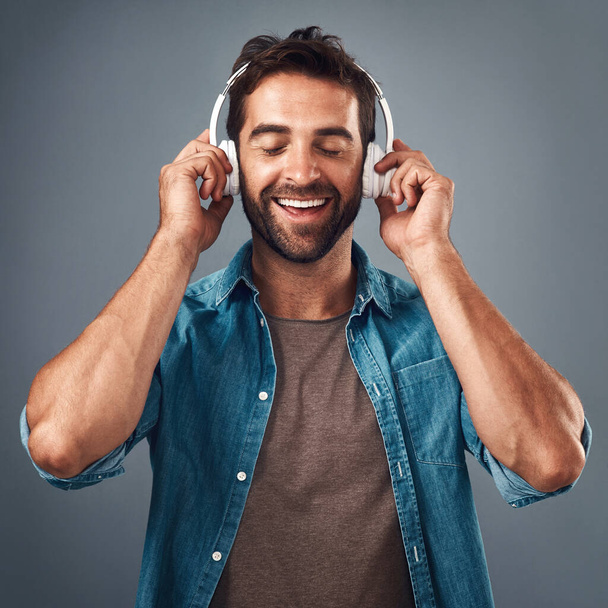 Коли музика вражає вас у почуттях. Студійний знімок красивого молодого чоловіка в навушниках на сірому фоні
 - Фото, зображення