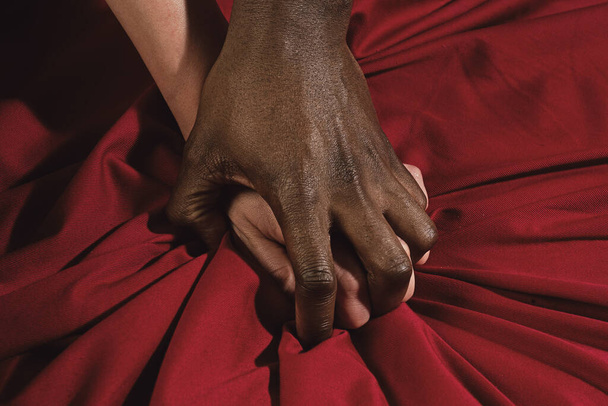 Passion in bed. African american and caucasian couple hands pulling white sheets in ecstasy, closeup. Couple making love in bed, foreplay of two hands. Female and male hands in love. Sexy hand touch - Foto, imagen