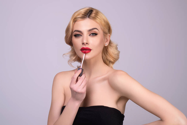 Beautiful young woman applying red lipstick on lips, studio color background. Sexy girl applied lipstick. Young nodel holding pink lipstick. Red lips make up. Beautiful woman putting lipstick on lips - Foto, Imagem