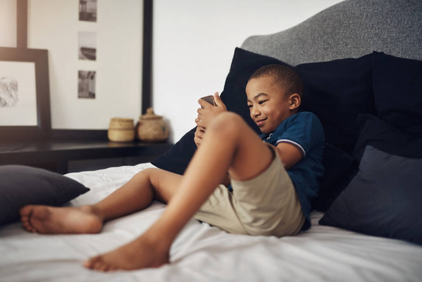 Im excited for some online fun. a young boy using a cellphone while sitting on his bed - Фото, зображення