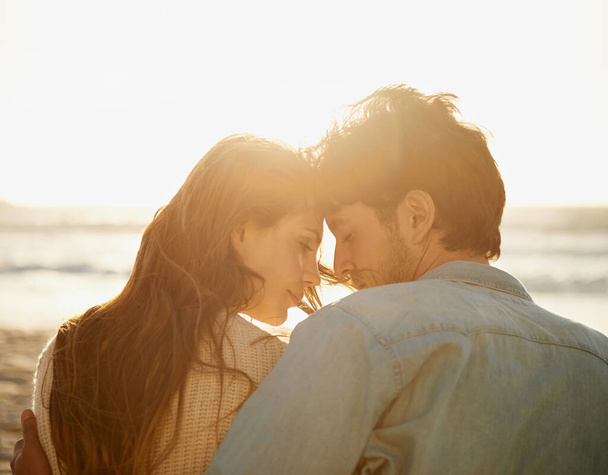 Intim und nah am Strand. Rückansicht eines liebenden jungen Paares, das eng beieinander am Strand sitzt - Foto, Bild